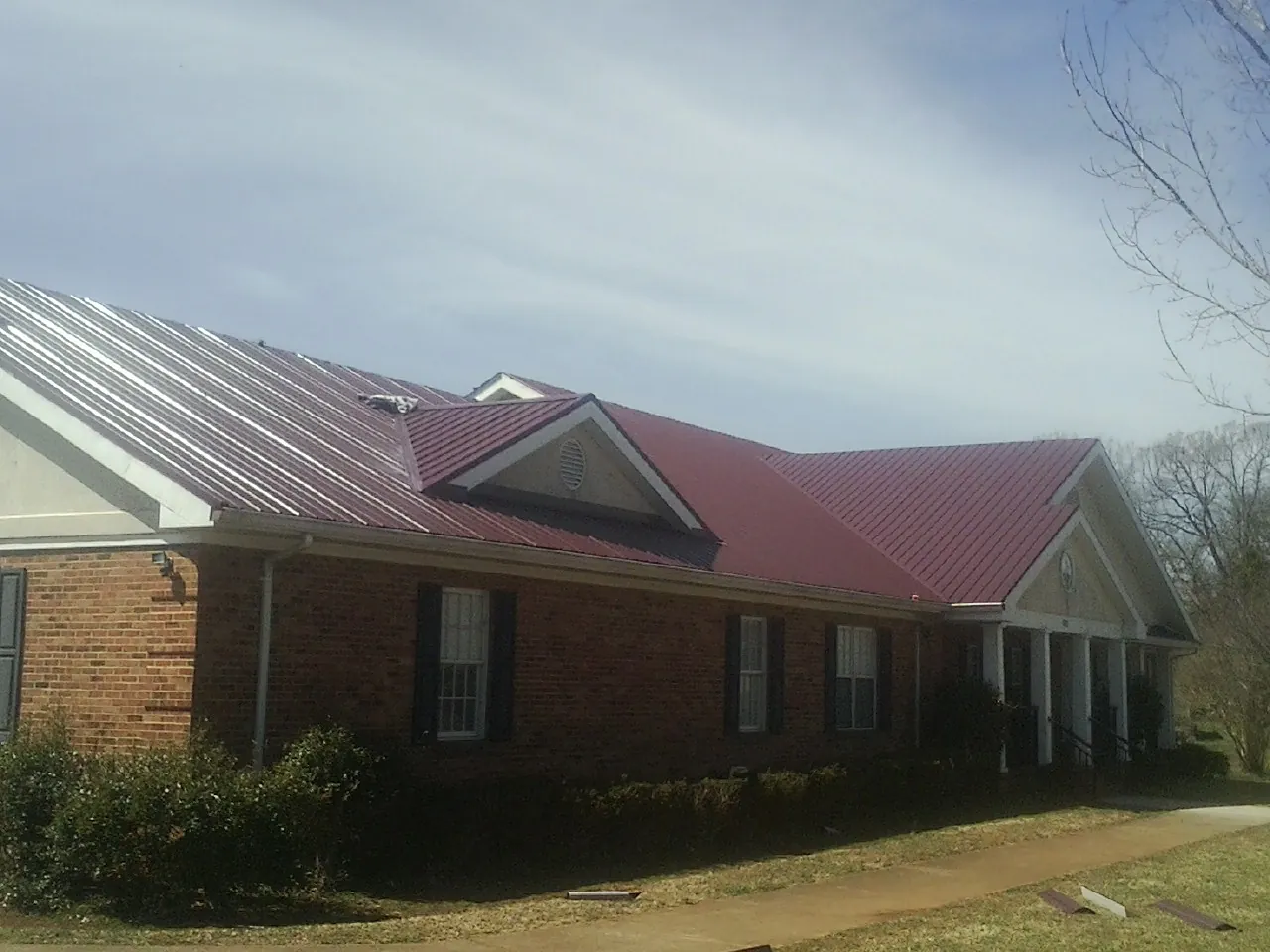 Red metal roof with gabled entries on a long brick building, from a Hail Damage Roof Repair job in Shandaken
