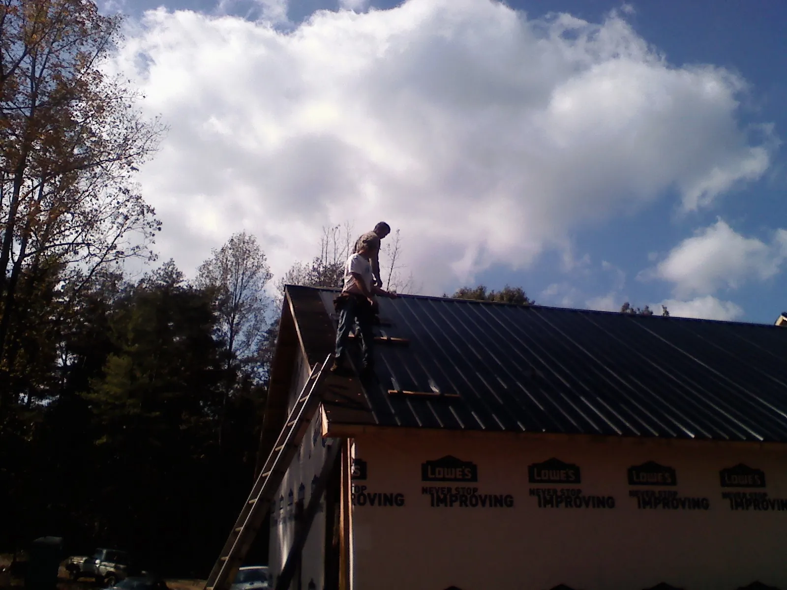 Roofer fastening dark metal panels high against a cloudy sky, from a Roof Inspection job in Shandaken