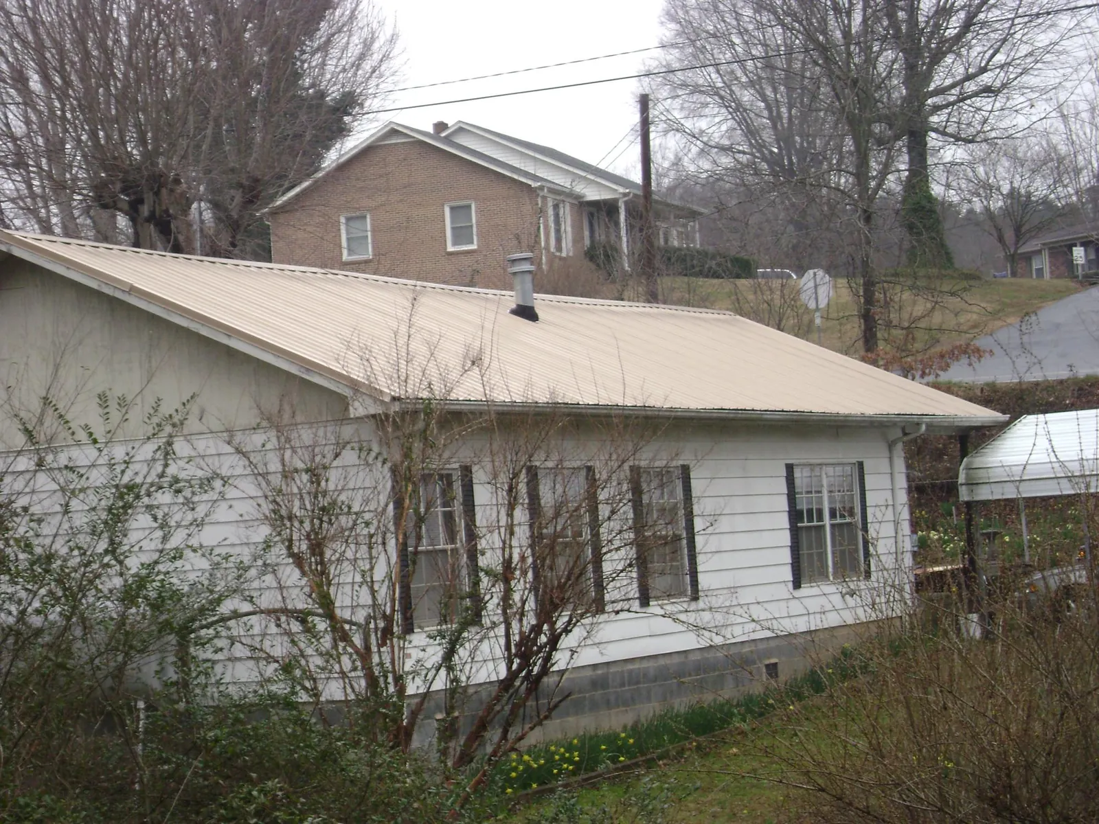 Tan metal roof on a white sided house set into a hillside — Commercial Roofing by Roofing Brothers in Shandaken